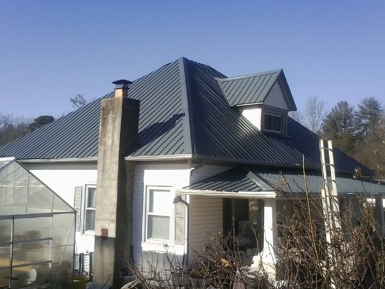 Dark blue standing seam metal roof on a white farmhouse with dormer — Slate & Tile Roof Repair by Roofing Brothers in Hesperia