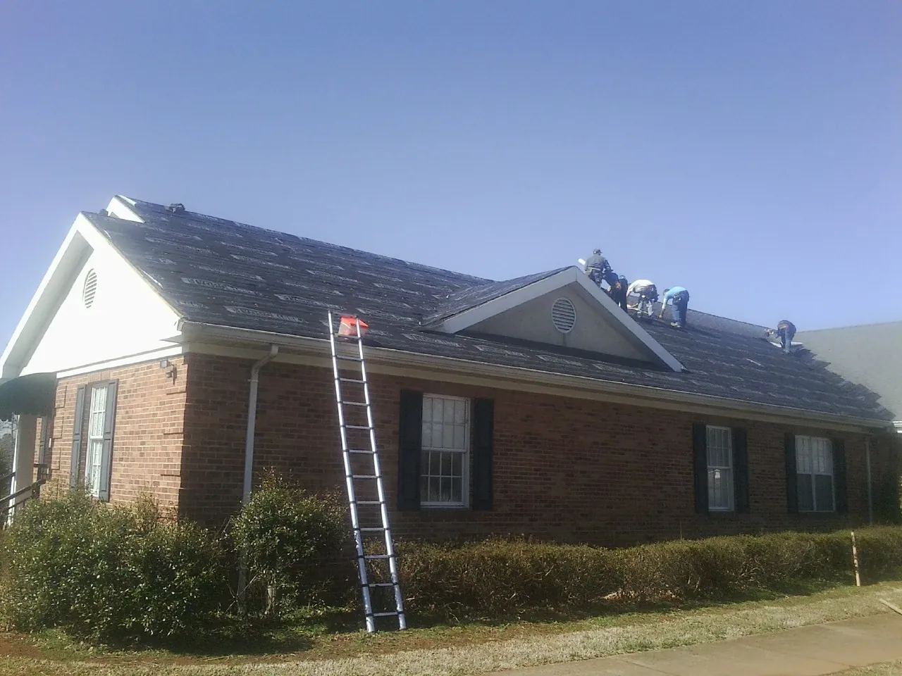 Crew tearing shingles off a brick ranch roof with a ladder set — Emergency Roof Repair work by our crew in Hesperia