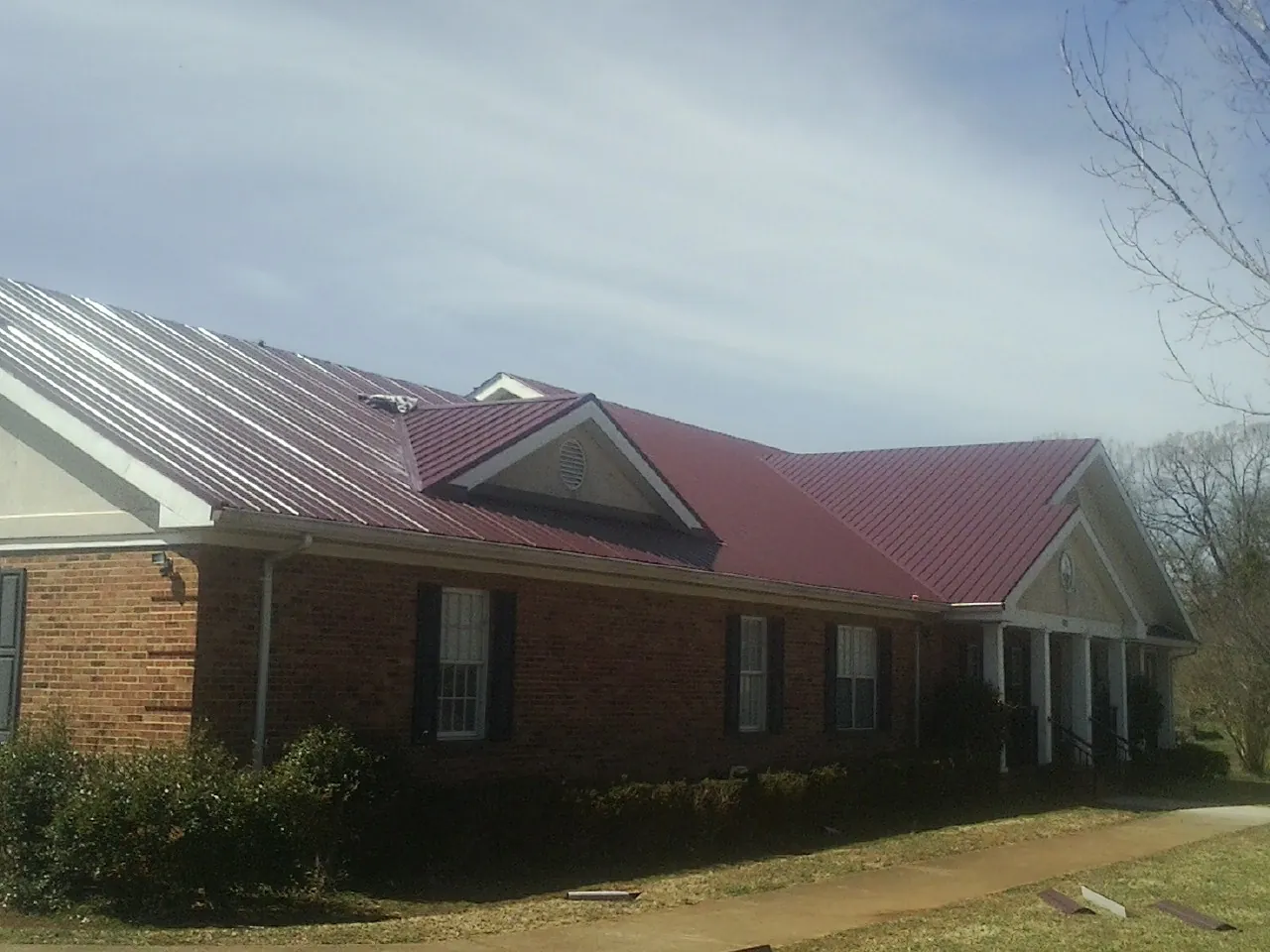 Red metal roof with gabled entries on a long brick building, from a Hail Damage Roof Repair job in Hesperia