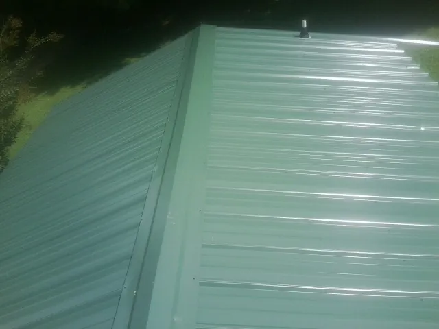 New green metal panels meeting at the ridge of a roof — Flat Roof Repair work by our crew in Hesperia